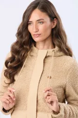 Campera beige con capucha y cordones ajustables, combinada en su parte superior con tejido de corderito y en su parte inferior con diseño capitoné. Cuenta con cierre frontal y broches a presión, además de bolsillos laterales.