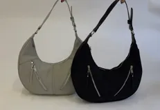Cartera mediana tipo hobo de cuero sintético color gris, con diseño semicircular, dos bolsillos externos frontales con cierre y correa de hombro ajustable.