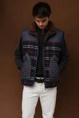 Chaleco acolchado con diseño combinado en tela lisa azul marino y tejido a cuadros estilo tweed con líneas rojas y blancas, cuello alto con forro interno de corderito marrón y bolsillos frontales con cierre.