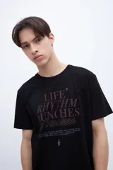 Remera negra de manga corta con cuello redondo. Presenta una estampa central en color bordó con la frase "LIFE RHYTHM PUNCHES Awakes" y un arte chico en la espalda.