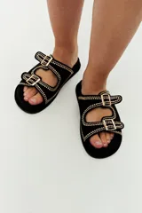 Sandalias planas negras con doble tira con hebilla y tachas doradas.