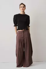 Blusa negra con cuerpo fruncido tipo smock, mangas cortas abullonadas con puños elásticos y volados en el cuello y el ruedo.