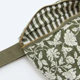 Riñonera de diseño acolchado en color verde kaki con estampado floral blanco. Cuenta con cierre superior metálico dorado y correa ajustable de cinta tejida al tono.