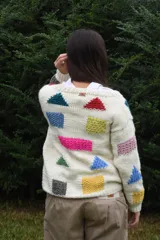 Cardigan de lana merino tejida a mano con dos agujas, color blanco con diseño de figuras geométricas en tonos multicolor y cierre frontal con botones de madera.