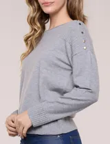 Buzo de punto fino color gris, de calce relajado, escote redondo amplio y canesú con textura acanalada. Cuenta con apliques de tachas metálicas doradas en la línea del hombro, mangas largas de hombro caído y puños y ruedo acanalados.