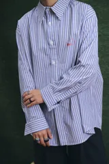 Camisa de corte oversize con estampado a rayas verticales en tonos azul y blanco, cuello clásico y cierre frontal con botones.