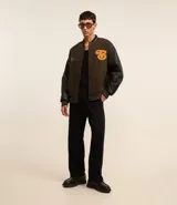 Campera bomber de estilo college con cuerpo a cuadros en tonos marrones y mangas largas de cuero sintético negro. Presenta cuello, puños y cintura acanalados a rayas, cierre abotonado, bolsillos laterales y aplique bordado de letra "B" en el pecho.