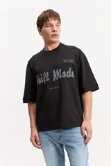 Remera negra de corte oversize, con mangas cortas amplias y cuello redondo ribeteado. Cuenta con una estampa frontal con la leyenda "Shift Mode" en tonos grises y texto secundario.