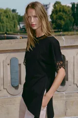 Camiseta negra de algodón con cuello redondo, manga corta y detalle de aplicación de encaje a tono en los puños. Presenta un diseño con bajo asimétrico y frunce lateral.
