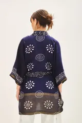Saco tipo kimono de estilo artesanal, confeccionado en tela azul marino con estampado geométrico y floral en blanco y detalles metalizados. Presenta solapas anchas, mangas largas, lazo ajustable en la cintura y bolsillos laterales.