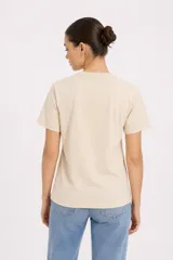 Remera de manga corta color beige, con cuello redondo y diseño al cuerpo. Presenta un estampado frontal multicolor de estilo veraniego con temática marina y detalles con glitter.