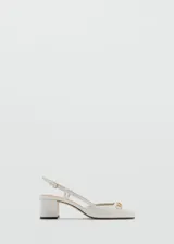 Zapato tipo slingback color blanco con tacón bloque de 5 cm, punta cuadrada y detalle de eslabones dorados en el empeine. Cuenta con cierre de hebilla ajustable en la tira trasera.