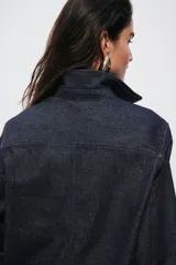 Camisa de denim de algodón rígido en color azul oscuro, con cuello clásico, cierre frontal de botones, bolsillos de parche en el pecho, mangas largas con puños abotonados y bajo redondeado.