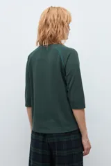 Remera de manga tres cuartos con diseño raglán y detalle de costura decorativa en los hombros. Presenta cuello redondo y un corte clásico.