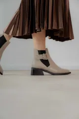 Botineta de cuero charol negro con acabado brillante, diseño de punta fina y taco cuadrado. Presenta un panel elástico lateral y una correa decorativa con hebilla metálica plateada.