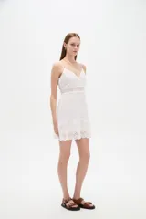 Vestido corto blanco de algodón con diseño de broderie, escote en V y tirantes finos. Presenta detalles de encaje y botones frontales.