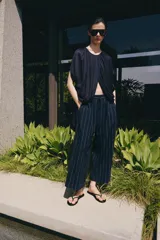 Pantalón de tiro medio confeccionado en mezcla de lino, con diseño de rayas verticales. Presenta cintura con trabillas, bolsillos laterales, pinzas en el delantero y cierre frontal con cremallera y botón.