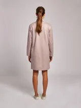 Vestido corto de jersey en color beige, con cuello subido y manga larga. Presenta un corte recto y minimalista.