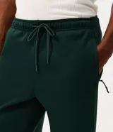 Pantalón deportivo de corte recto color verde oscuro, confeccionado en tejido de algodón y poliéster. Cuenta con cintura elástica con cordón ajustable, bolsillos laterales funcionales y una cinta decorativa lateral.