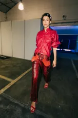 Pantalón de cuero rojo con estampado de serpiente en negro, de corte recto y tiro medio. Incluye detalles de parches de gamuza naranja en los laterales de la cintura.