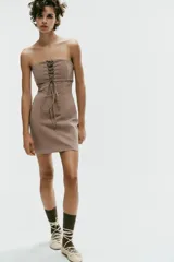 Vestido mini taupe de escote palabra de honor y hombros descubiertos, con detalle de tejido superpuesto y tiras cruzadas ajustables en el pecho. Cuenta con cierre lateral con cremallera oculta.