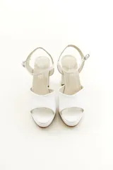 Sandalias de taco grueso y plataforma delantera, confeccionadas en cuero vacuno blanco, con tira ancha en la parte delantera y tira ajustable al tobillo con hebilla metálica.