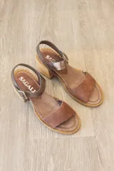 Sandalia de cuero marrón con tira frontal en cuero y correa al tobillo metalizada con hebilla ajustable. Cuenta con tacón ancho y bajo de acabado símil madera.