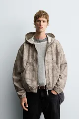 Cazadora negra de algodón con efecto lavado, corte relajado y capucha ajustable. Presenta cierre frontal de cremallera, bolsillos frontales tipo canguro y elásticos en puños y bajo.