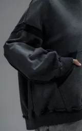 Hoodie oversize de corte crop en color gris oscuro con efecto desgastado. Presenta costuras expuestas, detalles de roturas en el ruedo y en la capucha, y bolsillos frontales con bordes reforzados.