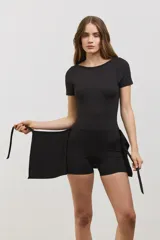 Vestido deportivo corto de color negro, diseñado para pádel. Presenta una estructura superior tipo remera de manga corta con espalda abierta, y una parte inferior que combina una calza corta con una media pollera envolvente que se ata en la cintura. Confeccionado en tejido suave y elástico.