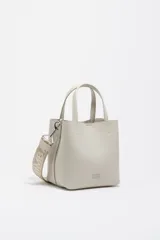 Bolso de mano de tamaño pequeño con estructura rígida, confeccionado en piel reconstituida color gris claro. Cuenta con doble asa superior, correa ajustable con logo de la marca y logo metálico en la parte frontal.
