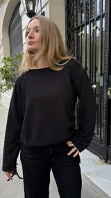 Buzo de punto negro con textura, de corte holgado y manga larga. Presenta un diseño ajustable en los laterales mediante tiras que permiten modificar el largo de la prenda.