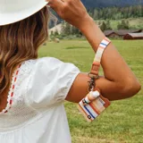 Llavero de muñeca con correa de tela a rayas multicolor, presilla de cuero sintético marrón con detalle grabado y gancho metálico.