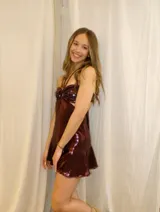Vestido corto de color bordó metalizado, con diseño strapless, escote halter y argolla central en el busto con detalles de lentejuelas. Presenta aberturas cut-out en la cintura y falda corta con vuelo.