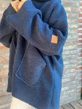 Campera de corderito color verde oscuro, con diseño holgado, cuello alto y manga larga. Presenta una etiqueta de cuero sintético en la manga.