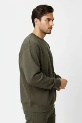 Buzo de cuello redondo color verde militar, de mangas largas con puños y dobladillo acanalados, y calce holgado.