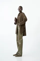 Camisa larga de manga larga, color marrón oscuro, con cuello camisero y botones frontales. Presenta un corte holgado y frunce sutil en las mangas.