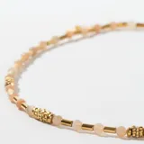 Gargantilla dorada con cuentas de piedra natural color durazno y detalles de acero dorado.