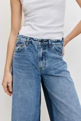 Jean wide leg de tiro medio, confeccionado en denim azul con detalles de paneles laterales en un tono más oscuro, tiro medio, cierre frontal con botón y cremallera, y diseño de perneras amplias.