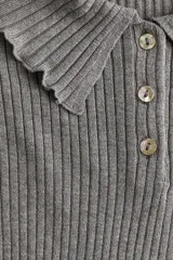 Buzo tipo polo de punto acanalado color gris, con cuello clásico, tapeta con tres botones nacarados y terminaciones con ribetes sobrehilados en puños y ruedo.