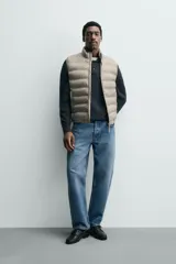 Chaleco acolchado verde oscuro, con cuello alto, cierre frontal con cremallera y bolsillos laterales. Confeccionado en tejido técnico repelente al agua.