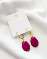 Aros colgantes con aro dorado y dije de resina color fucsia.