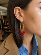 Aros tipo argolla dorados con diseño calado de filigrana y colgantes de pequeñas cuentas rojas en el borde inferior.
