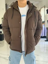 Campera puffer impermeable color beige con capucha desmontable con cordones negros, cierre frontal con cremallera y solapa con botones a presión.