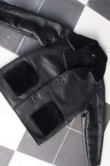 Gamulán de cuero negro con interior de piel sintética, corte oversize, solapas grandes, cierre frontal con botones y bolsillos laterales con apliques de piel.