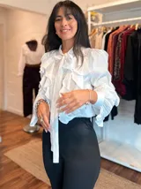 Camisa negra de tela liviana con diseño de volados verticales en el frente y mangas, cuello con lazo ajustable y puños con botones.