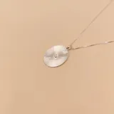 Gargantilla plateada con dije circular con diseño de rayos y una circonia en el centro.