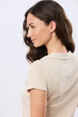 Remera polo de algodón color beige con mangas cortas, escote en V y cuello camisero. Presenta delicados mini bordados florales distribuidos en toda la prenda.