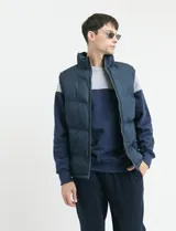 Chaleco capitoneado de color azul marino con cierre frontal completo y cuello alto. Presenta un diseño acolchado con costuras horizontales y forro interior con estampado escocés.