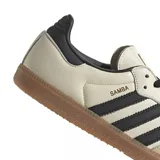 Championes Adidas modelo Samba OG, con diseño clásico de perfil bajo, parte superior de cuero en tono crema, icónicas tres tiras laterales en negro, refuerzo de gamuza en la puntera y suela de goma color caramelo.